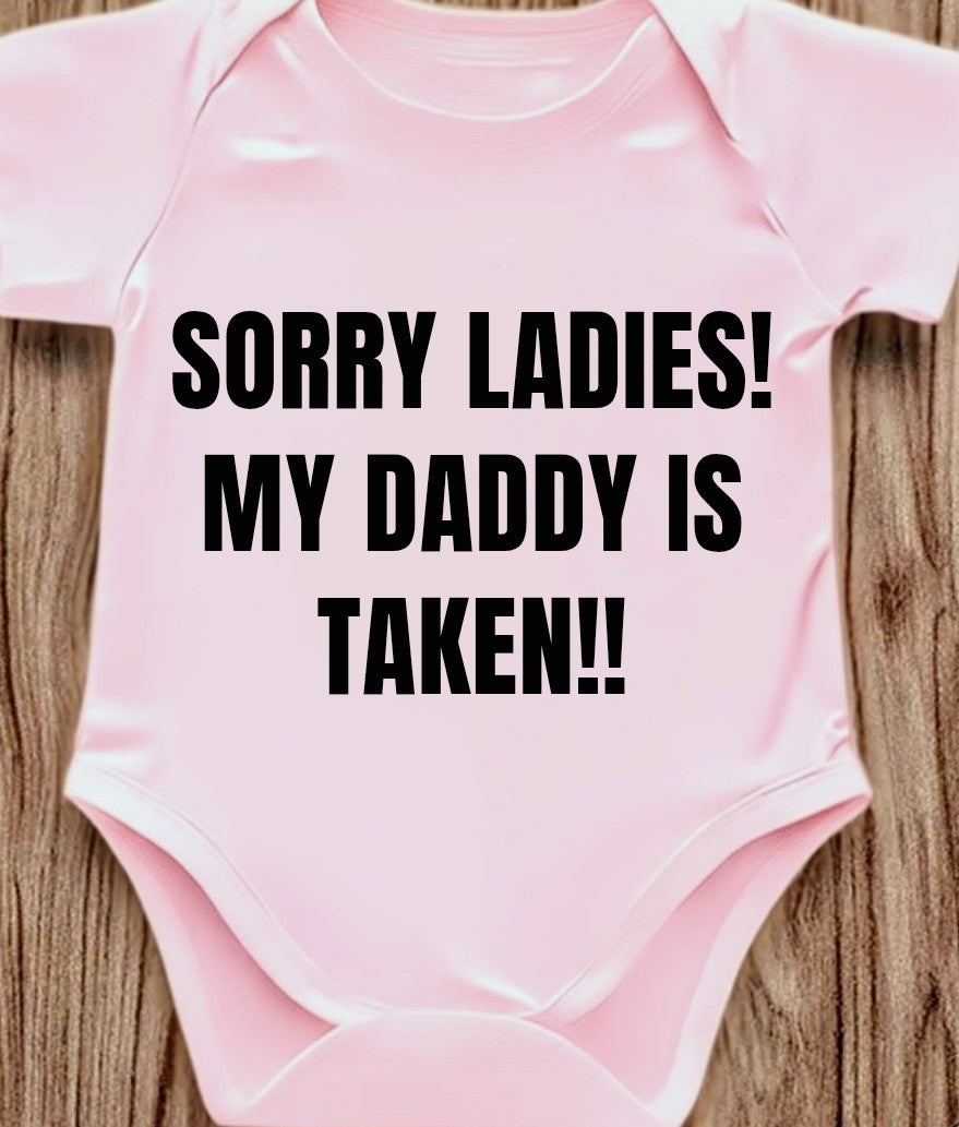 Funny baby onesie in pink with the phrase 'SORRY LADIES! MY DADDY IS TAKEN!!' printed in bold black letters.